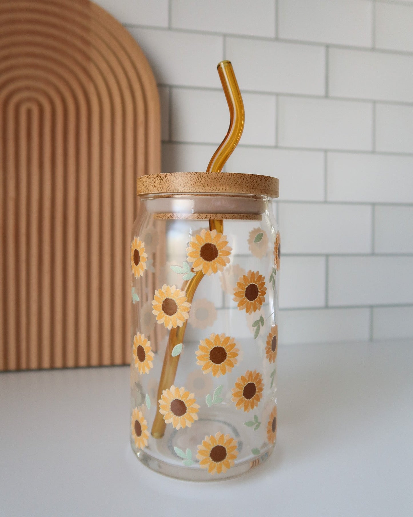 Glass tumbler with sunflower design and bamboo straw on a white surface.