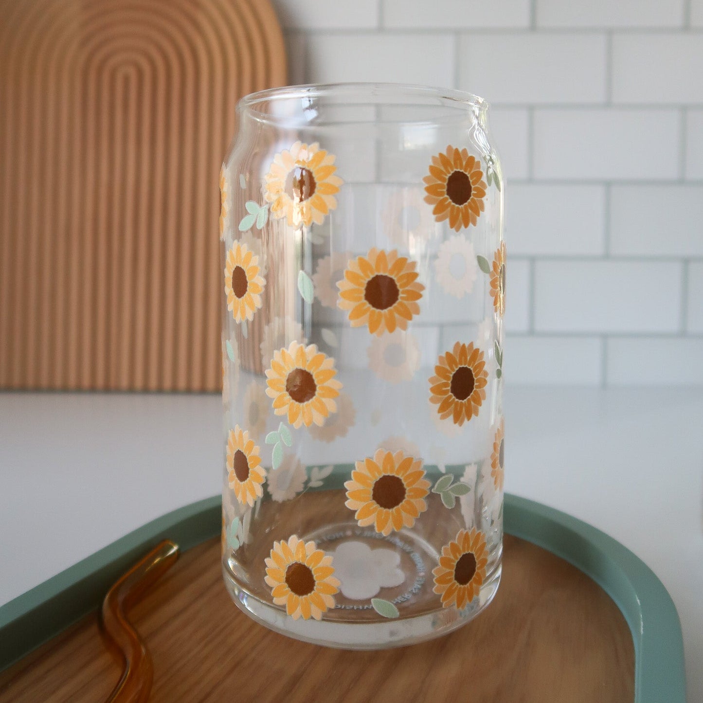 Clear glass with sunflower designs on a wooden surface with a white tiled wall background