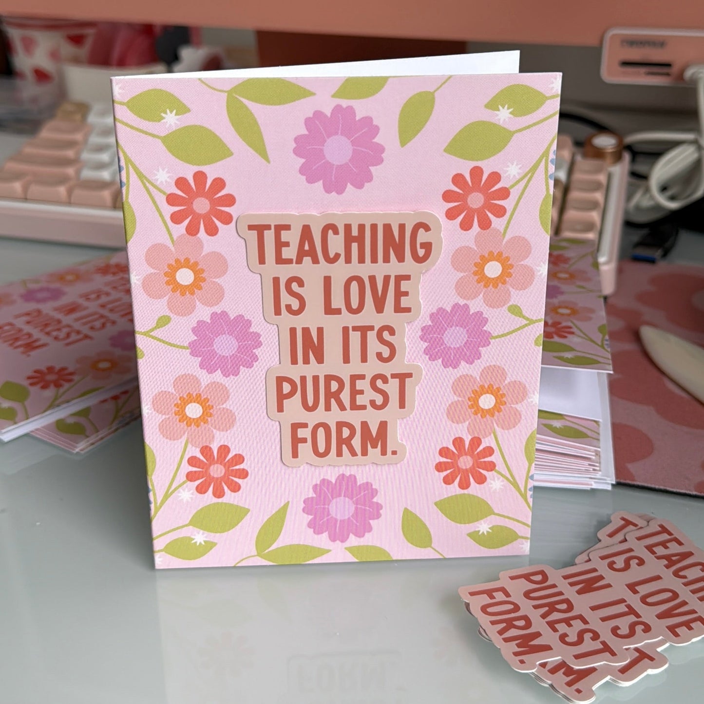 Card with floral design and text 'Teaching is love in its purest form' on a desk.