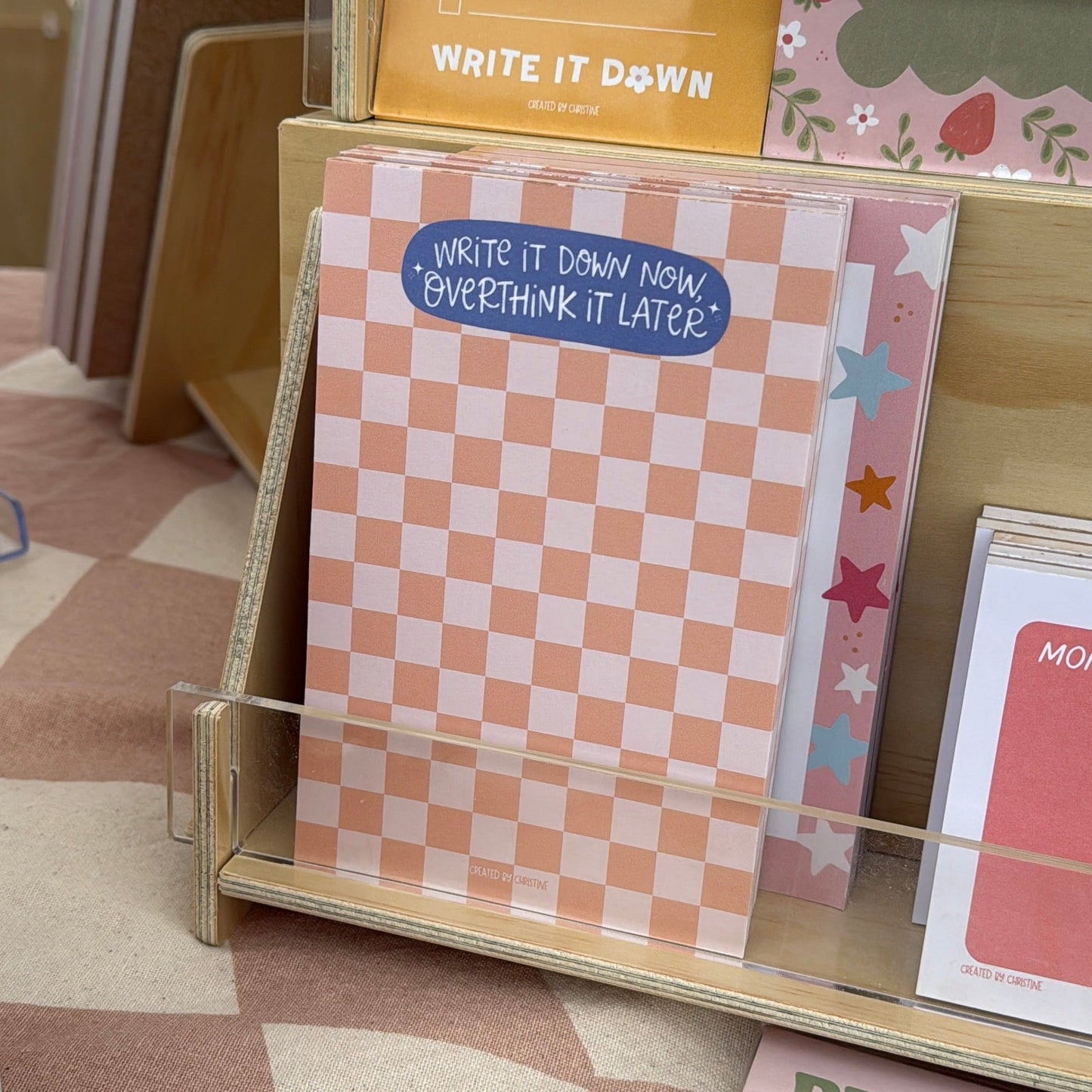 Stationery items including a yellow notepad, checkered notebook, and other stationery on a display stand.