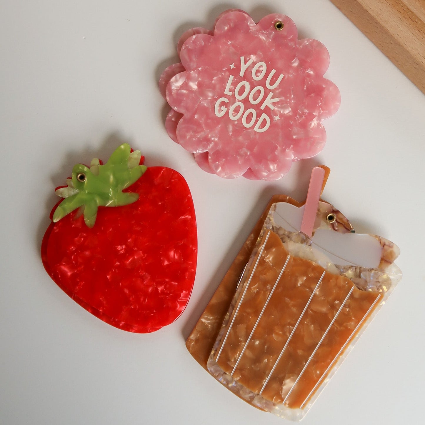 Three decorative items on a white surface: a red strawberry-shaped item, a pink heart-shaped item with 'YOU LOOK GOOD' text, and a brown popsicle-shaped item.