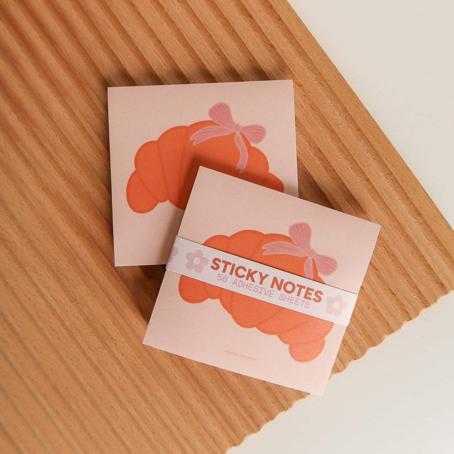 Two small pink sticky note books with cloud designs on a wooden surface.