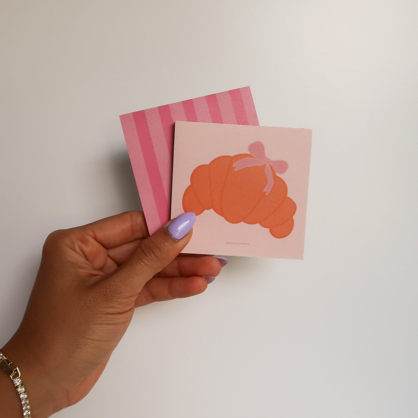 Hand holding two small pink cards with orange designs against a white background