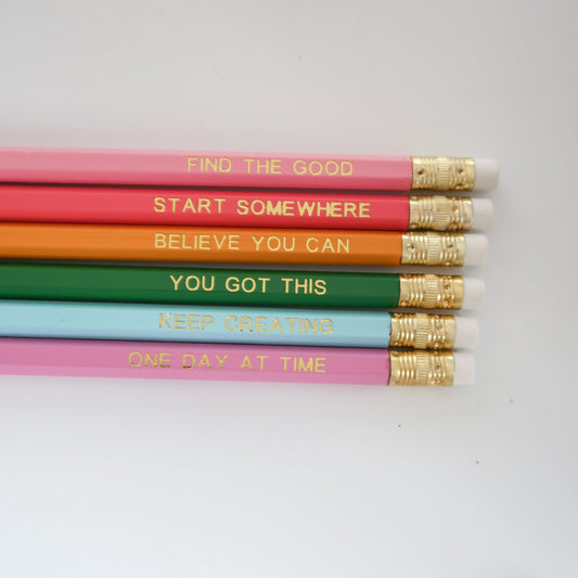 Six colorful pencils arranged horizontally on a white background, each printed with a positive phrase in gold foil and finished with white erasers and gold ferrules.