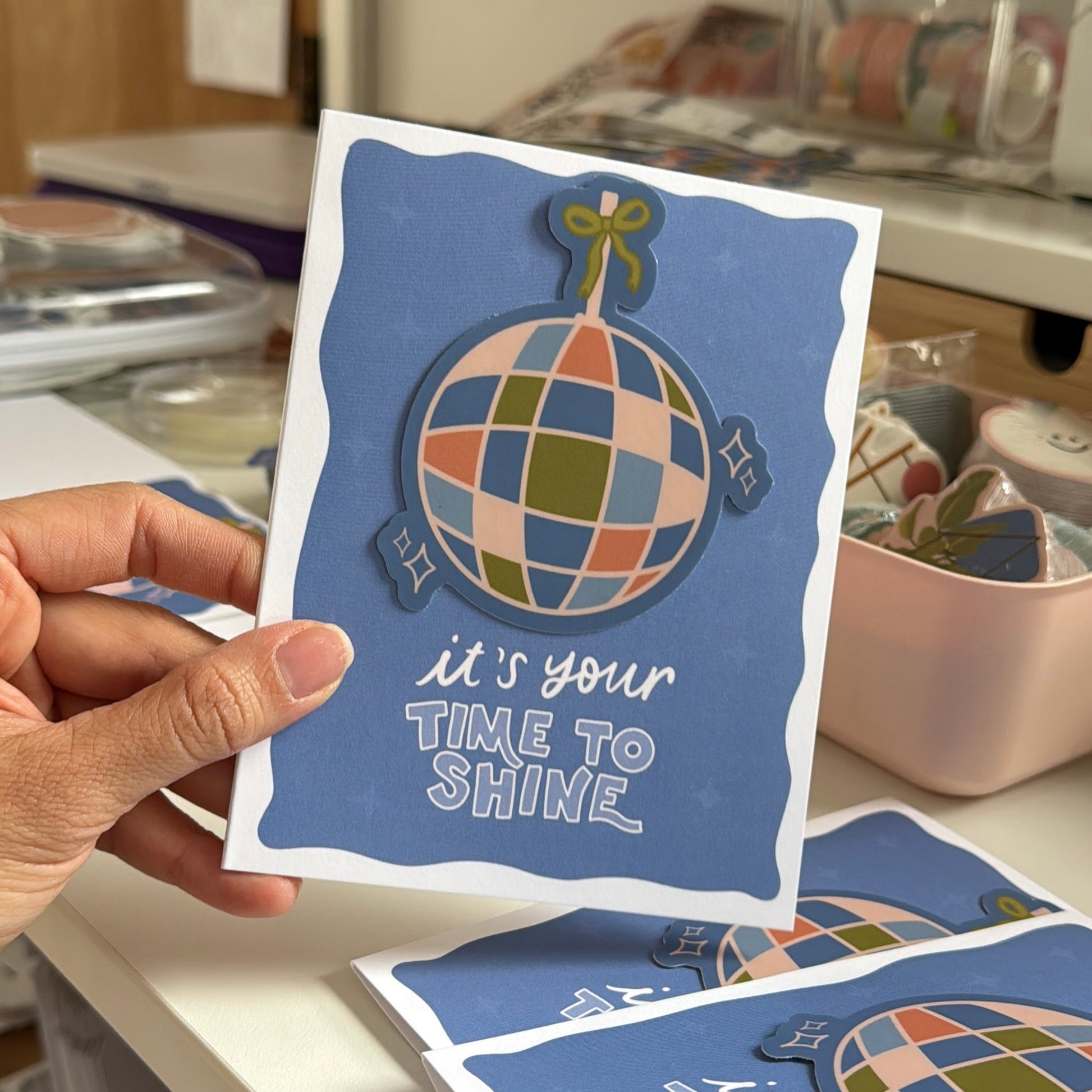 Hand holding a card with a colorful globe design and text in a craft setting.