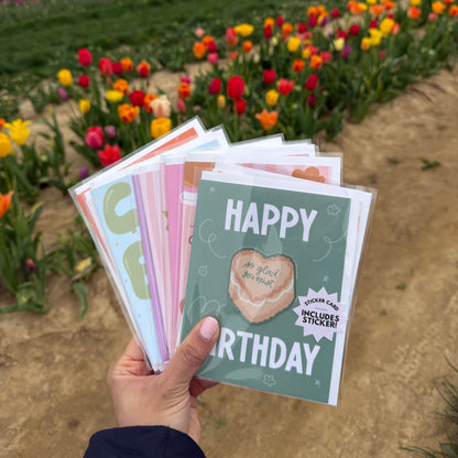 Hand holding a stack of greeting cards with a field of flowers in the background