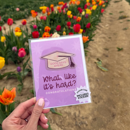 Hand holding a purple card with text and an illustration of a graduation cap against a background of flowers.