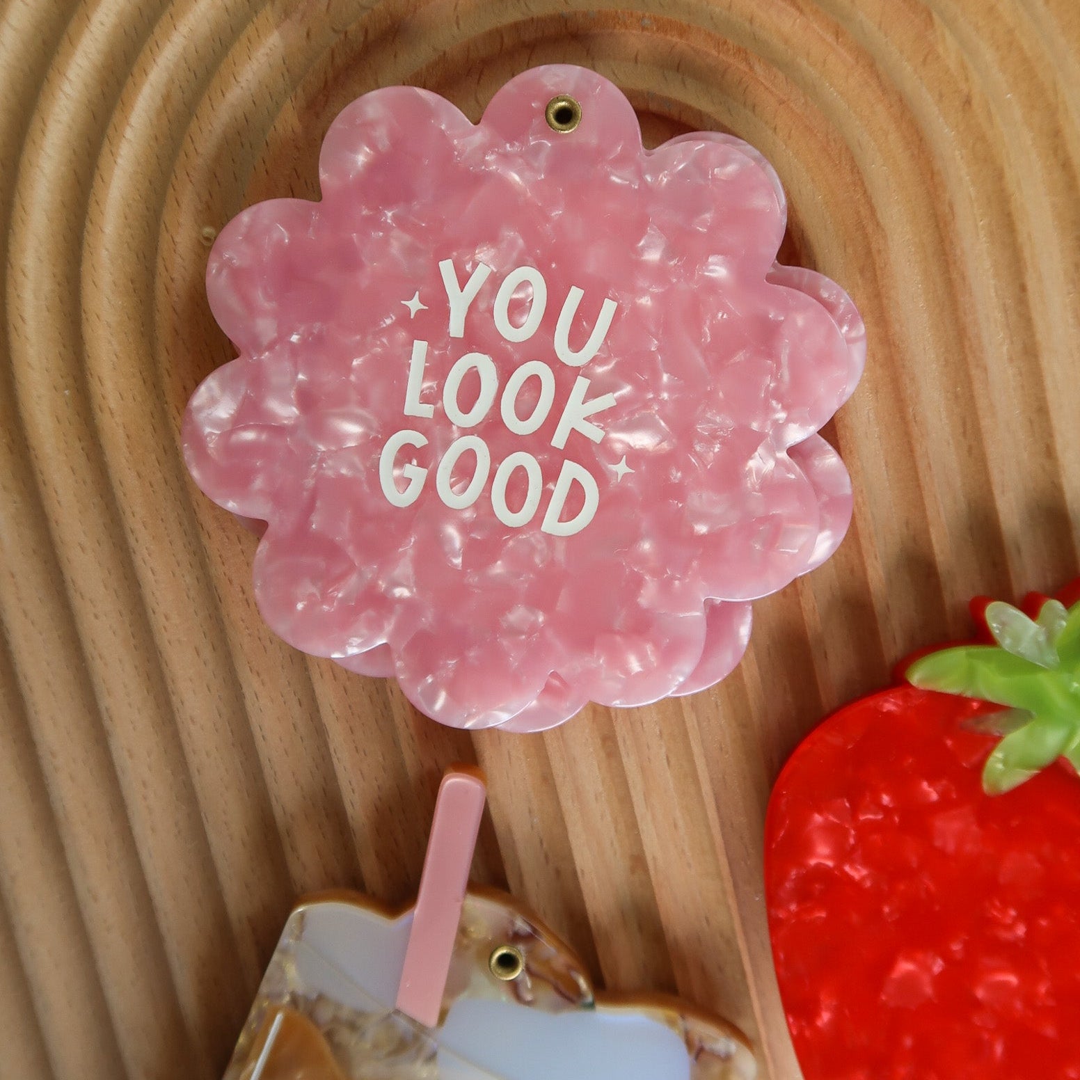 Pink flower-shaped hair clip with 'YOU LOOK GOOD' text on a wooden background