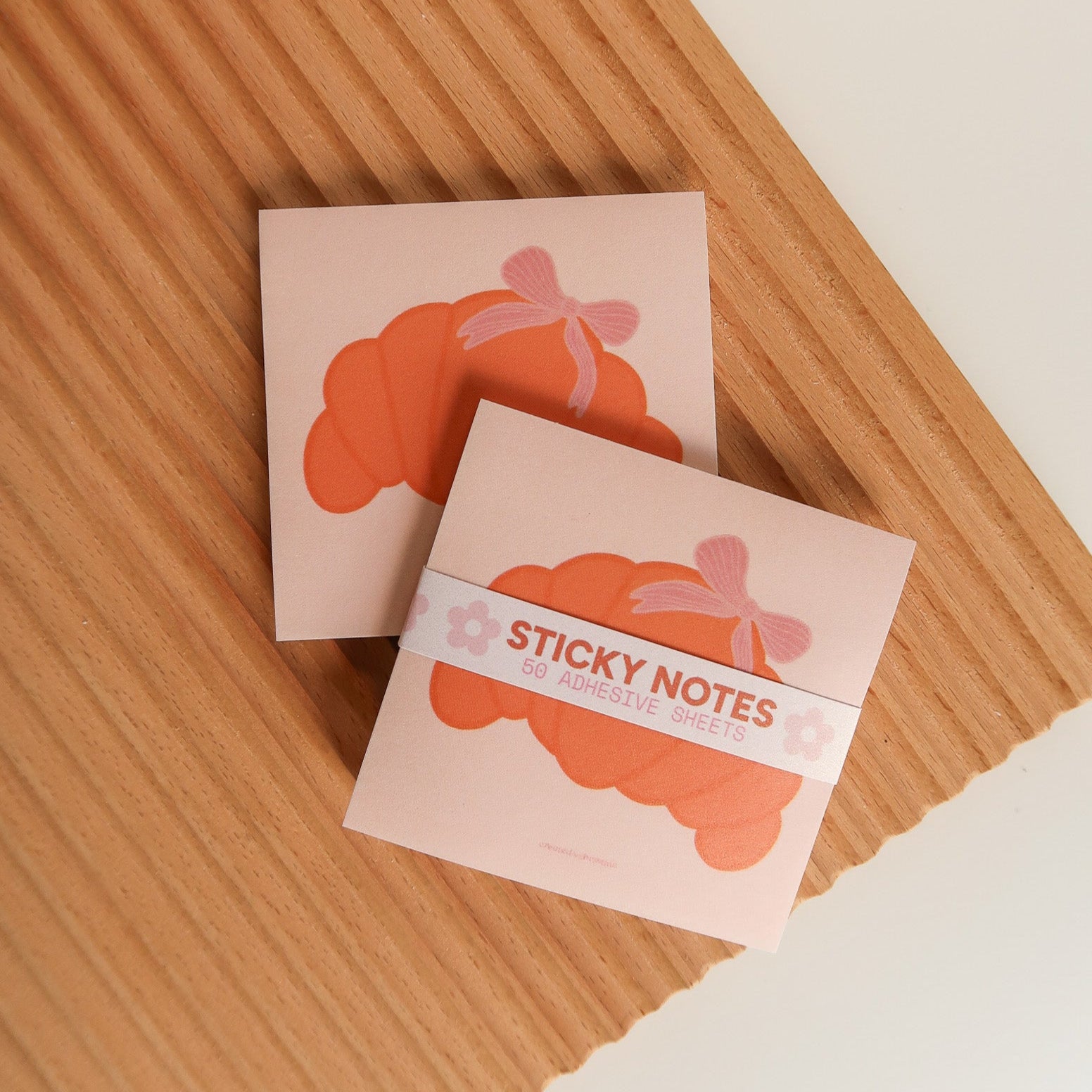 Two small pink sticky note books with cloud designs on a wooden surface.
