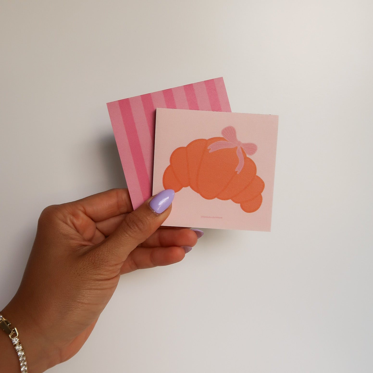 Hand holding two small pink cards with orange designs against a white background