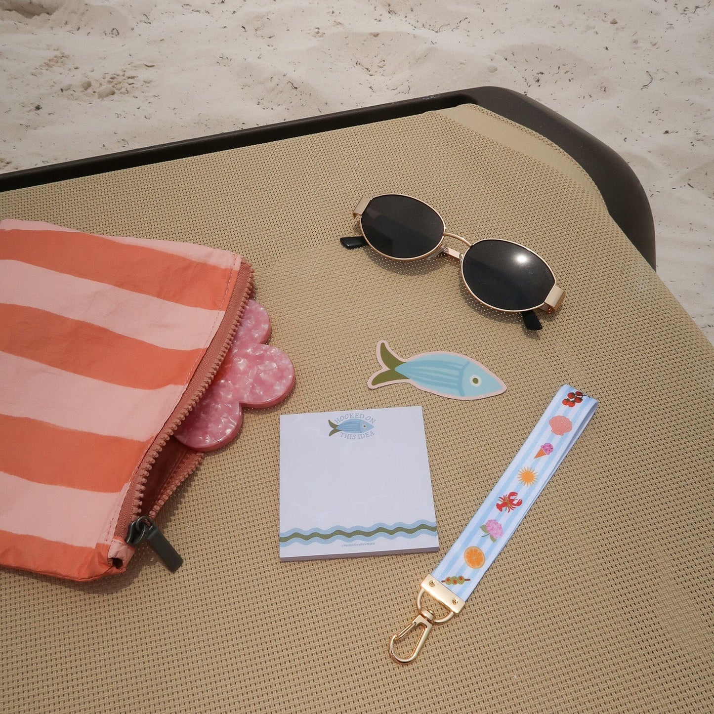 Sunglasses, notepad, fish-shaped magnet, and floral keychain on a textured surface